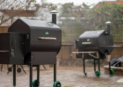 Two outdoor grills on a brick patio
