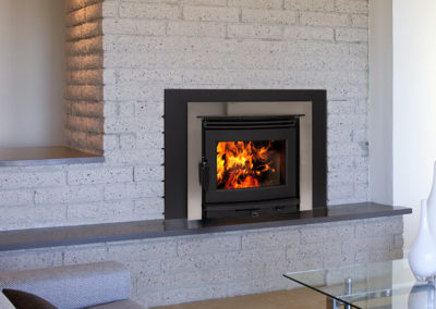 Wood burning insert fireplace in a gray stone wall